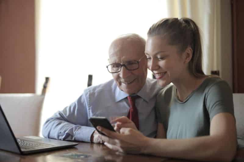 Younger woman helping a senior man on a mobile phone