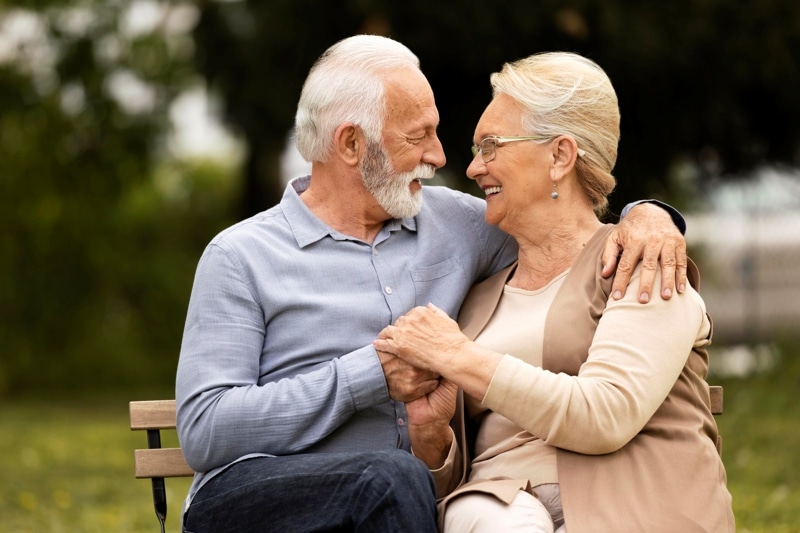 Senior couple smiling at each other on a park bench